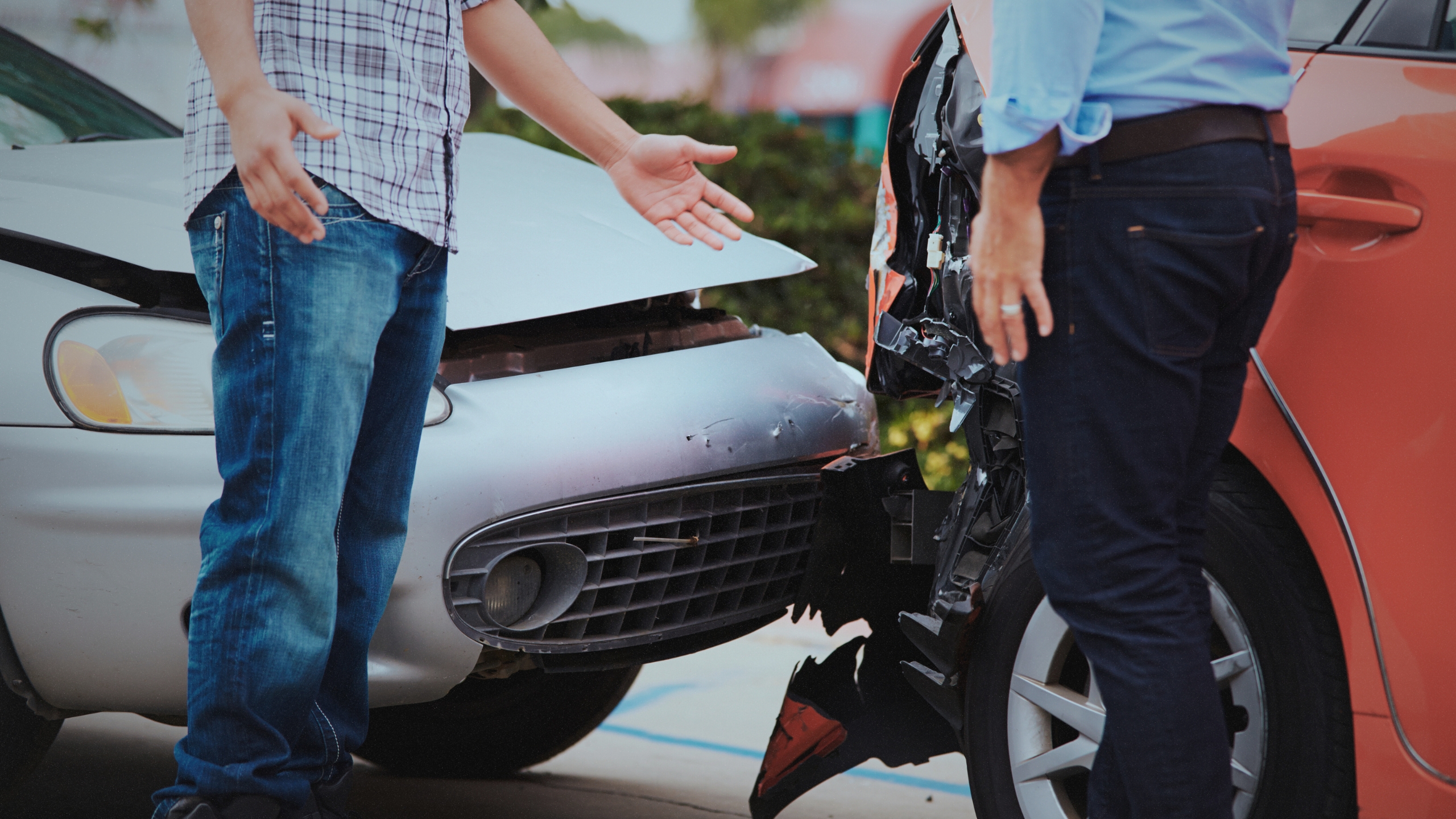 Two individuals visible from the waist down appear to negotiate after a fender bender, which is seen in the background,