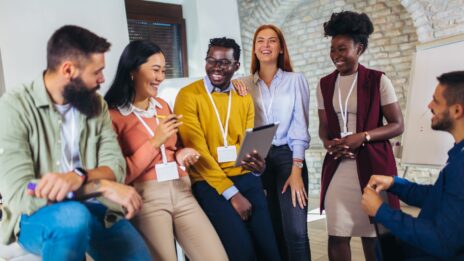 A diverse group of co-workers talk and laugh while facing the camera.