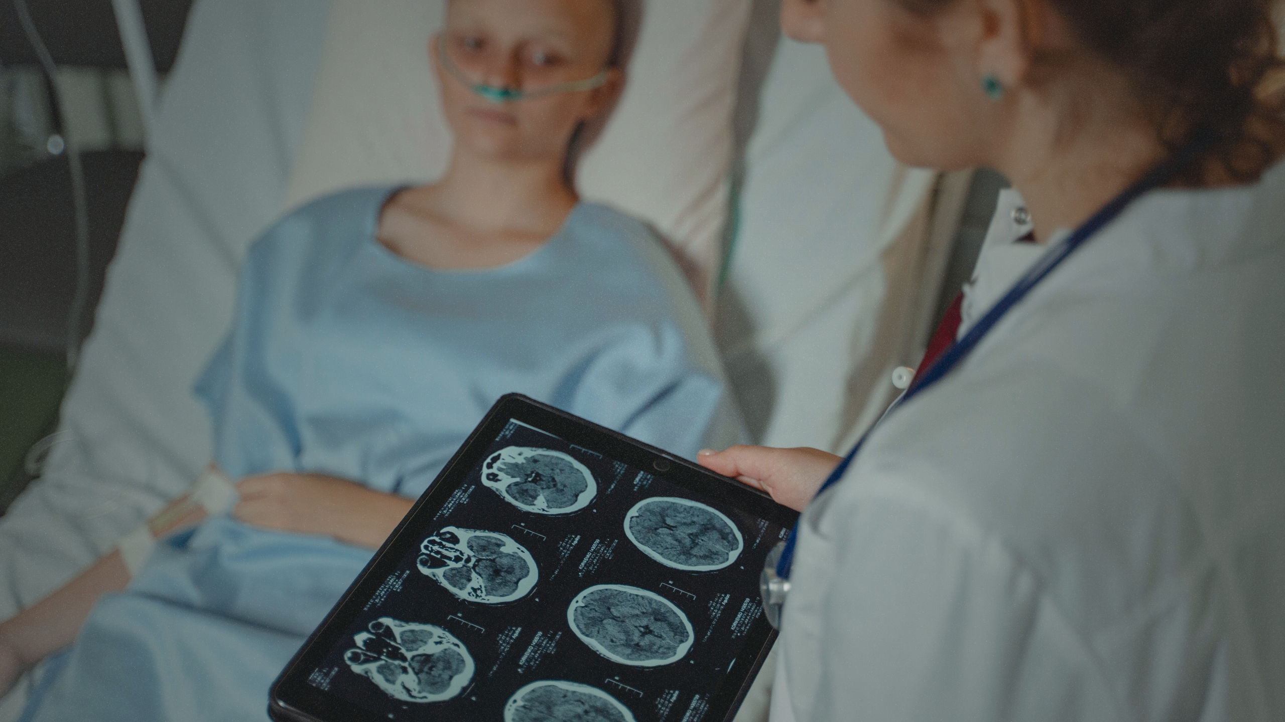An over-the-shoulder view of a brain scan chart being shown to a young patient in a hospital bed.