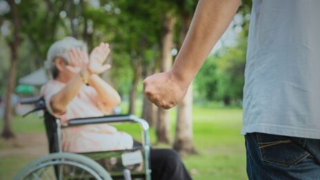Elder woman sitting in wheelchair in front of a man with a clenched fist.