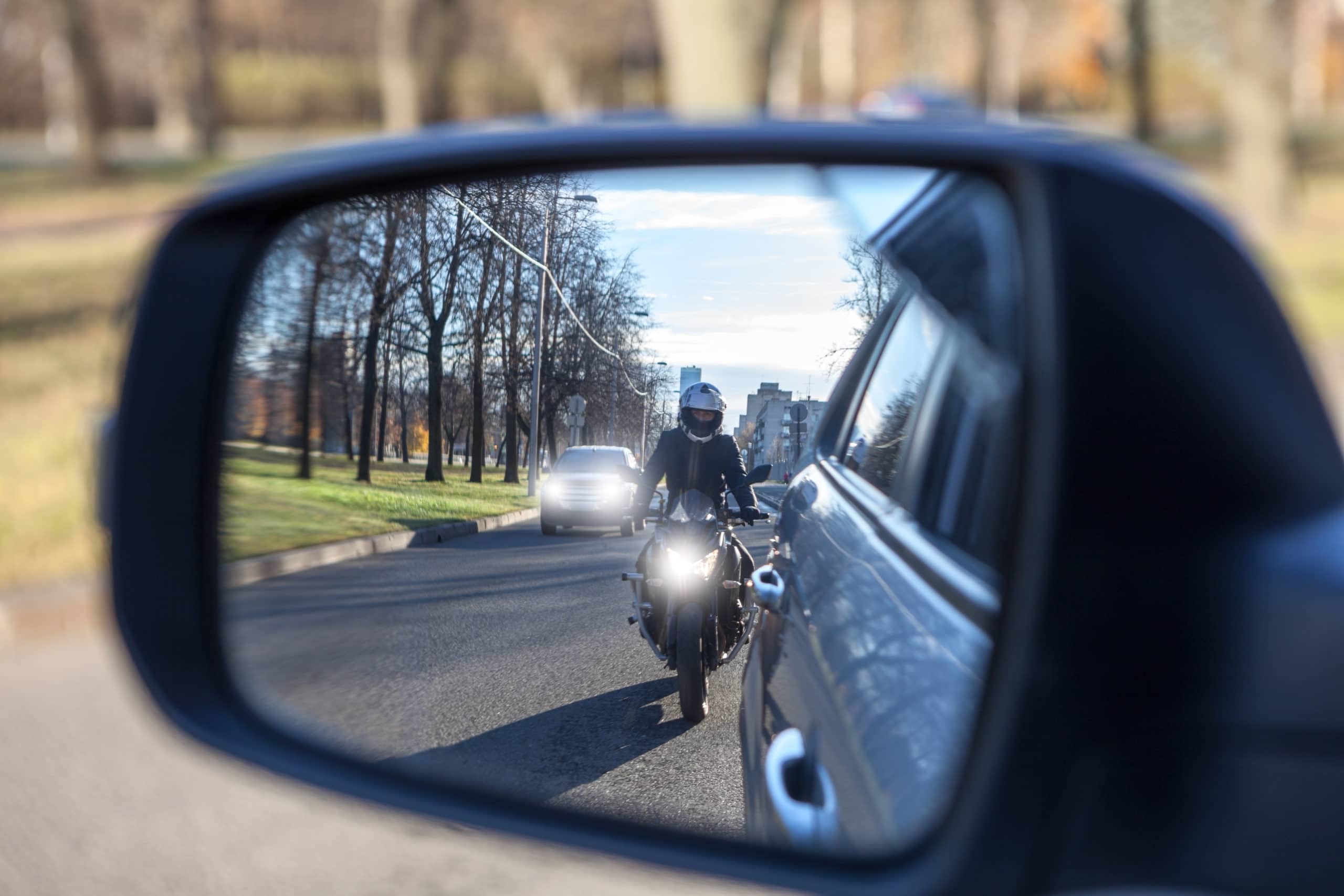 Motorcycle rider in review mirror of a car