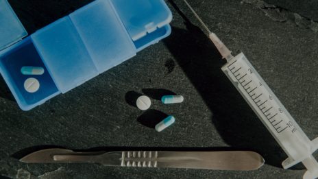 pills laying on table beside needle and scalpel