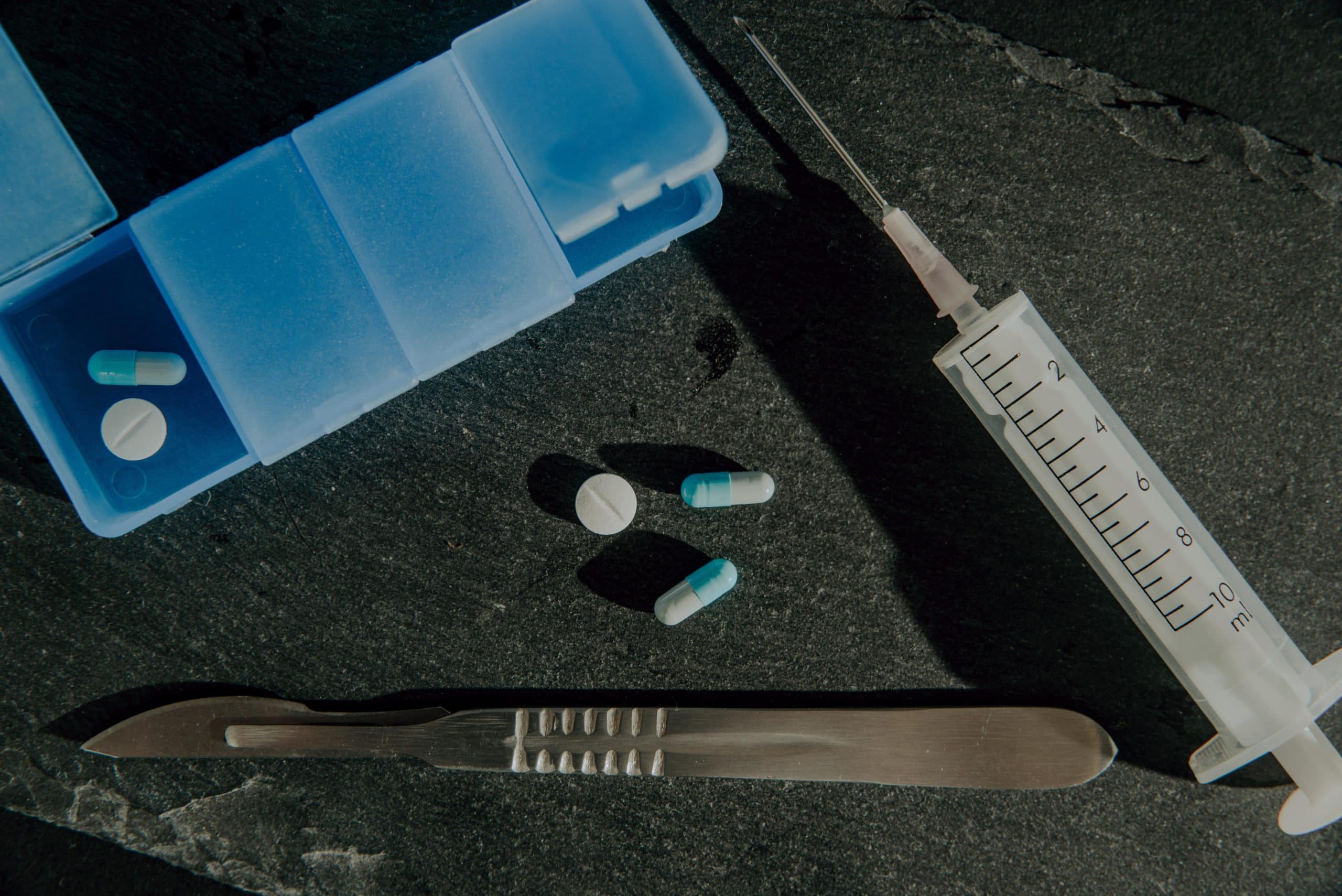pills laying on table beside needle and scalpel
