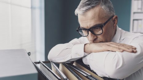 middle aged man look stressed over file cabinet