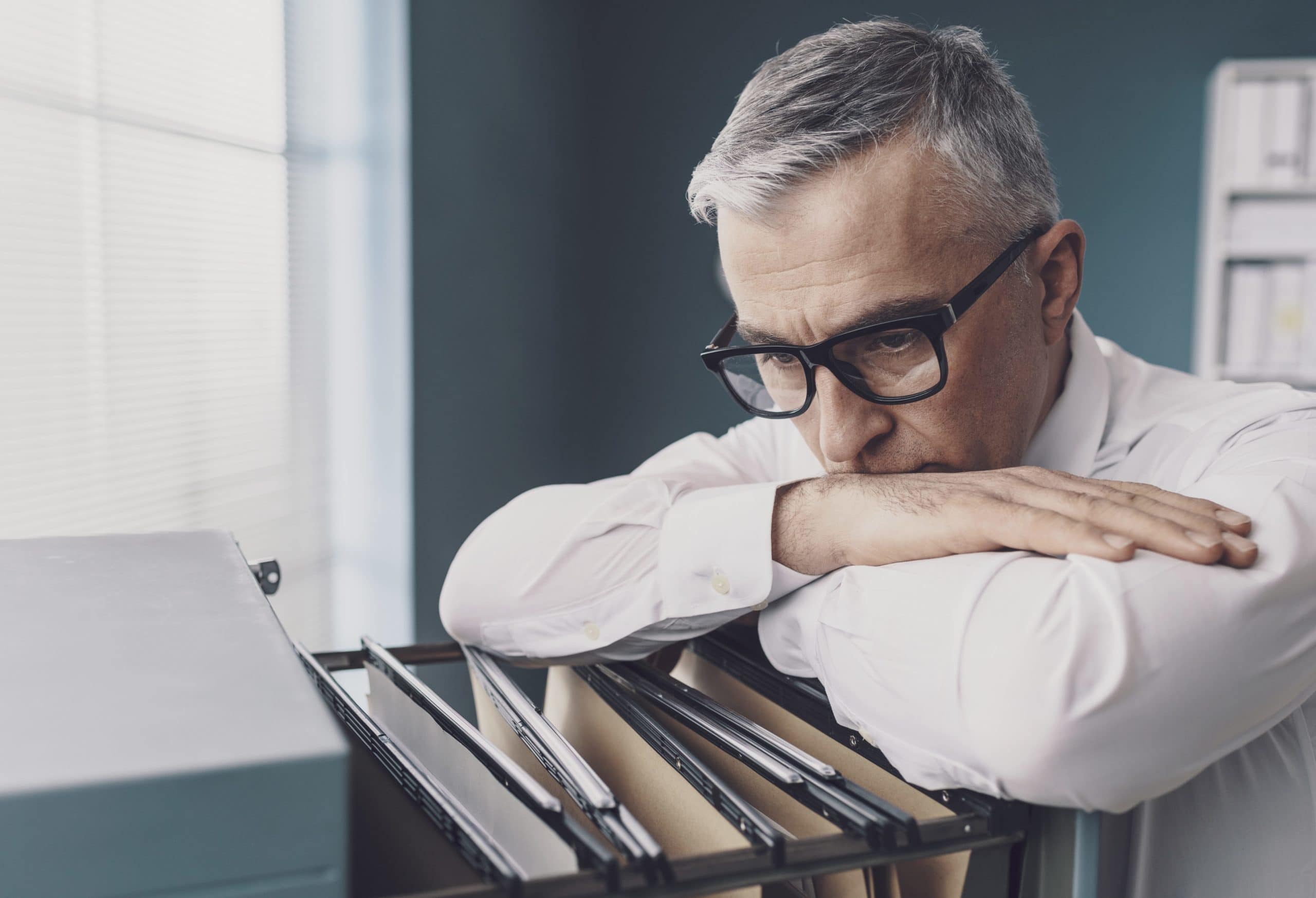 middle aged man look stressed over file cabinet