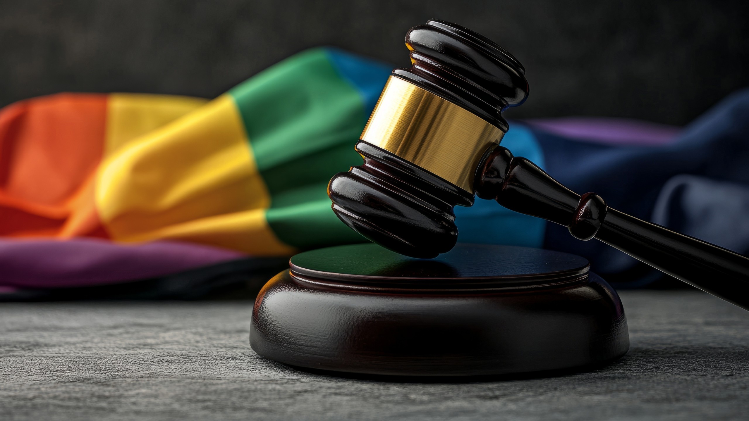 A gavel sits on a slate surface in front of a vivid rainbow Pride flag.