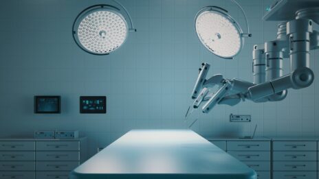 A robotic arm appears to "operate" on an empty table in a hospital room.