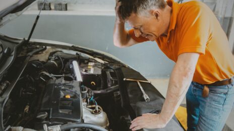 A distressed vehicle owner looks in on his car engine.