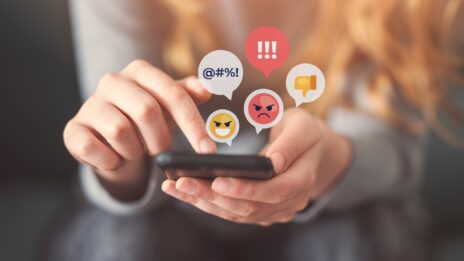 A close up of hands holding a phone with angry emoji bubbles floating above the screen.