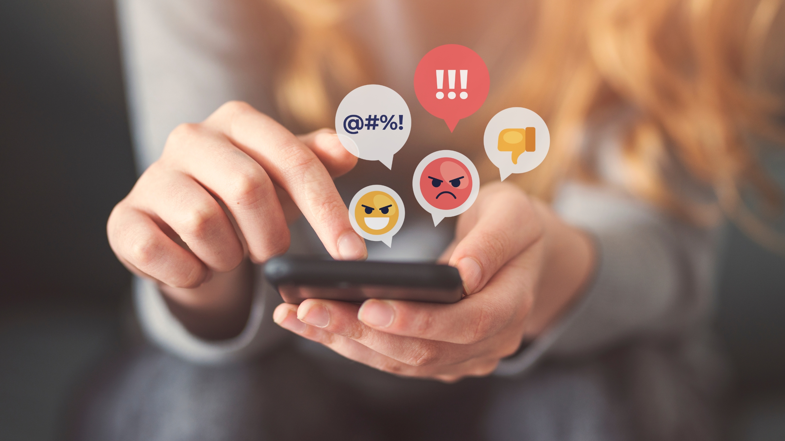 A close up of hands holding a phone with angry emoji bubbles floating above the screen.
