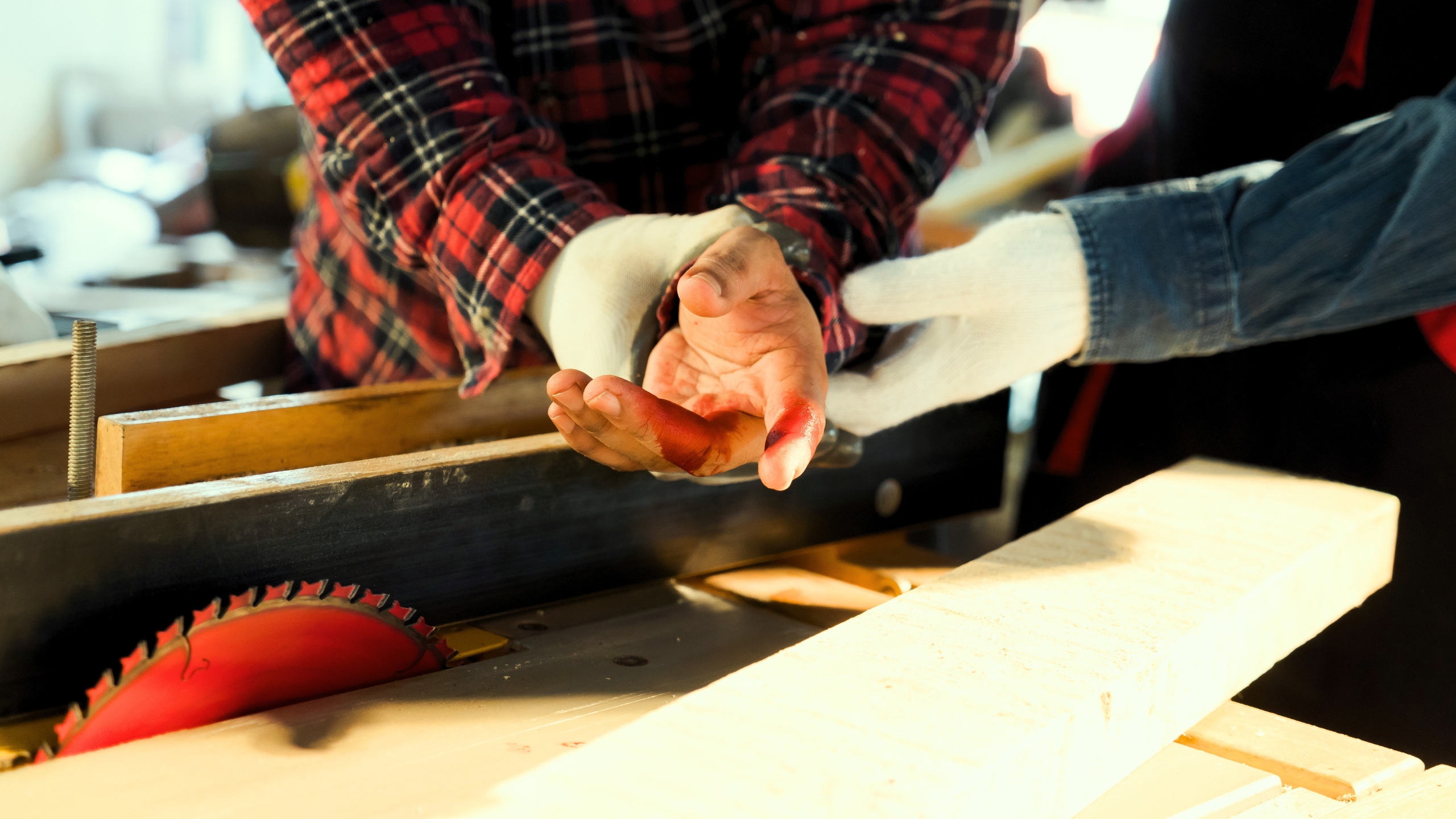 An injured finger in close up, with gloved hands examining and power tools and materials visible below.